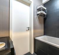 A bathroom in a 2-room apartment with dark tiles, a bathtub, and white towels.