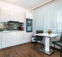 A kitchen with white cabinets, a dining table, and a wood-patterned floor in a two-room apartment.