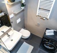 A bathroom in a 2-room apartment with a washing machine, toilet, and sink, decorated with plants.