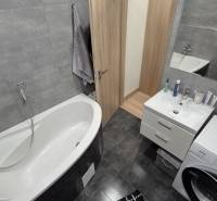 Bathroom in a 2-room apartment with a bathtub, mirror, washing machine, and gray tiles.