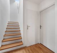 A hallway with white walls, wooden stairs, and a floor with a wood pattern, family house.