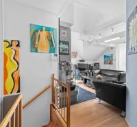 Living room with art paintings, black leather sofas, and a wooden staircase in a family house.