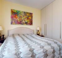 Bedroom in a family house with a large bed, colorful painting, and wardrobes.