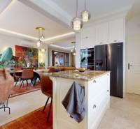 A kitchen with an island, light flooring, chairs, and artwork in a family house.