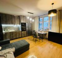 Living room with kitchen, gray sofa, wooden decor flooring, dining table, pendant lamps.