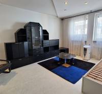 A room in a 3-room apartment with black furniture, a bed, and a chair.