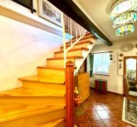 A staircase with a wooden decor, a dining table, a display cabinet, and a chandelier in a family house.