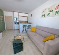 Studio apartment with wood-patterned flooring, a sofa, and bar stools.