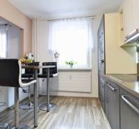 A kitchen with bar stools and a wooden decor floor in a 3-room apartment.
