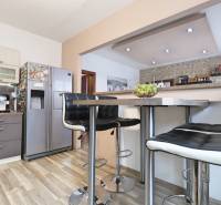 A kitchen in a 3-room apartment with bar stools, a stainless steel refrigerator, and a wooden decor floor.