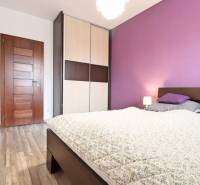 A bedroom with a purple wall and a wooden decor floor in a three-room apartment.