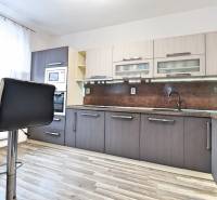 A kitchen with wood-patterned flooring in a 3-room apartment with built-in appliances and bar stools.