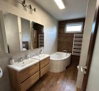 A bathroom in a family house with a wooden decor floor, a bathtub, and a double sink.