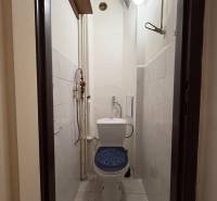 Narrow toilet with ceramic tiles and a wall light in a studio apartment.