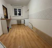 Kitchen in a studio apartment, wooden decor flooring, white tiles on the walls.