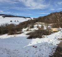 Snow-covered residential lands in Horná Mičiná with a panorama of hills and trees.