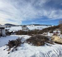 A snowy landscape with residential plots in Horná Mičiná, set in gentle hills.