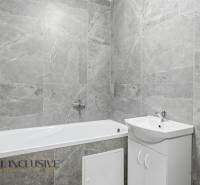 A bathroom with a bathtub and a sink in a three-room apartment with gray tiles.