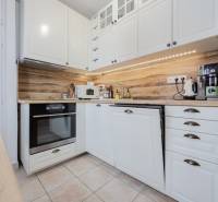 A kitchen in a 2-room apartment with a wood-patterned floor and white cabinets.