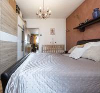 Bedroom in a 2-room apartment with a bed, wood-patterned floor, and a baby crib.