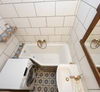 A bathroom in a 2-room apartment with a bathtub, washing machine, and unique tiles.