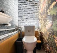 A small restroom with a sink, colorful wallpaper, and visible pipes in a dining area.