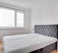 Bedroom with a large window, a simple bed, and a wooden decor floor in a 3-room apartment.