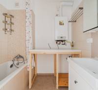 Bathroom with a bathtub in a 2-room apartment, with a wooden table and a gas boiler.