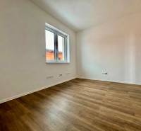 An empty room in a family house with white walls and a wooden-patterned floor.