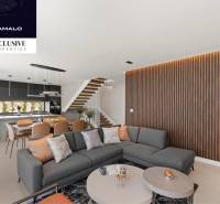 Interior of a villa with a corner sofa, open kitchen, and wooden decor on the wall.