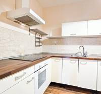 A kitchen in a 2-room apartment with white cabinets and a wooden decor floor.