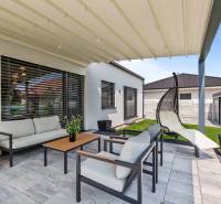 A terrace of a family house with seating and a swing, surrounded by a green lawn.