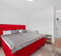A bedroom in a family house with a red bed and a wooden decor floor.