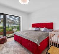 A bedroom in a family house with a large bed, a baby crib, and balcony doors.