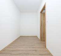 A hallway in a 2-room apartment with white walls and a wooden-patterned floor.