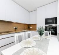 A kitchen in a 2-room apartment with white furniture and wooden decor.