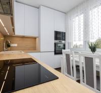 A kitchen in a 2-room apartment with a wooden decor, white cabinets, and a dining table.