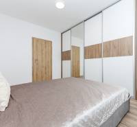 A bedroom with wood-patterned flooring and a large built-in wardrobe in a two-room apartment.