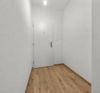 A hallway in a 3-room apartment with a wood-patterned floor and white walls.