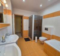 A bathroom with orange and white tiles, a shower corner, a bathtub, and a double sink in a family house.