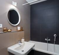 A bathroom in a 2-room apartment with a bathtub, a sink, and a round mirror above the sink.
