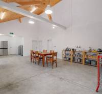 Interior of a building with a concrete floor, a table with chairs, and kitchen equipment.