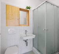 Bathroom in a building with white tiles, a shower stall, and a simple sink.