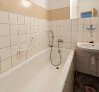 A bathroom with a bathtub and a sink in a two-room apartment, tiled with white tiles.
