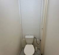 A toilet in a 3-room apartment with a window blind and tiled floor.