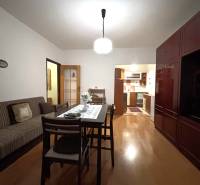 A two-room apartment with a wooden floor, a dining table, and a kitchen in the background.