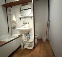 Bathroom in a studio apartment with a bathtub, sink, and floor with wooden decor.