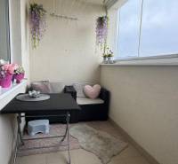 A furnished balcony with seating and hanging flowers in a 3-room apartment.
