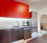 A kitchen unit with red cabinets, a dining table, and a view into the living room in a 3-room apartment.