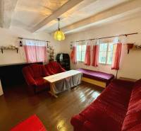 A living room in a cottage with red curtains, sofas, and a wooden decor floor.